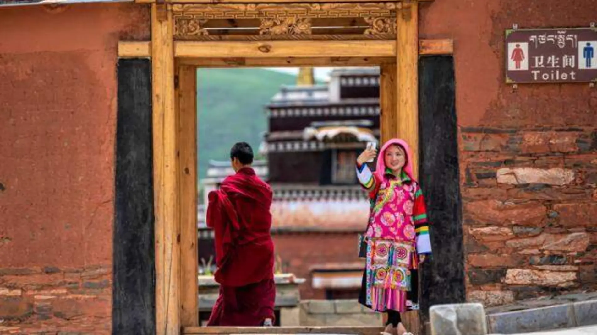 Tourist woman takes a picture while Tibetan Buddhist monk passes by at Labrang Monastery, in Xiahe County